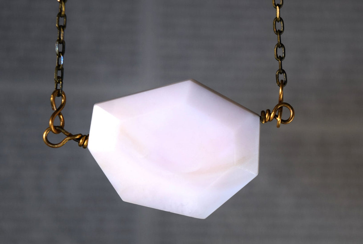 A faceted white pendant necklace with gold-toned chain and wire attachments, centered against a blurred gray background.